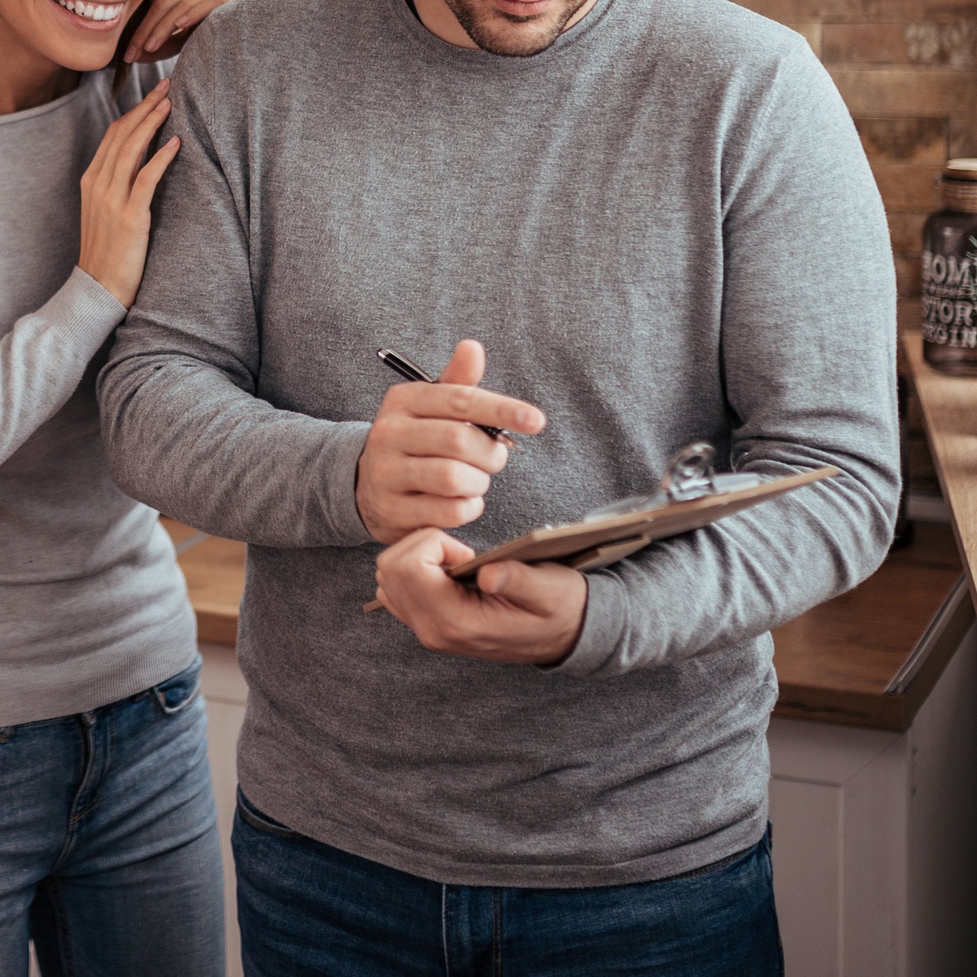 A future father and mother, both wearing grey, and making a plan on a clipboard.