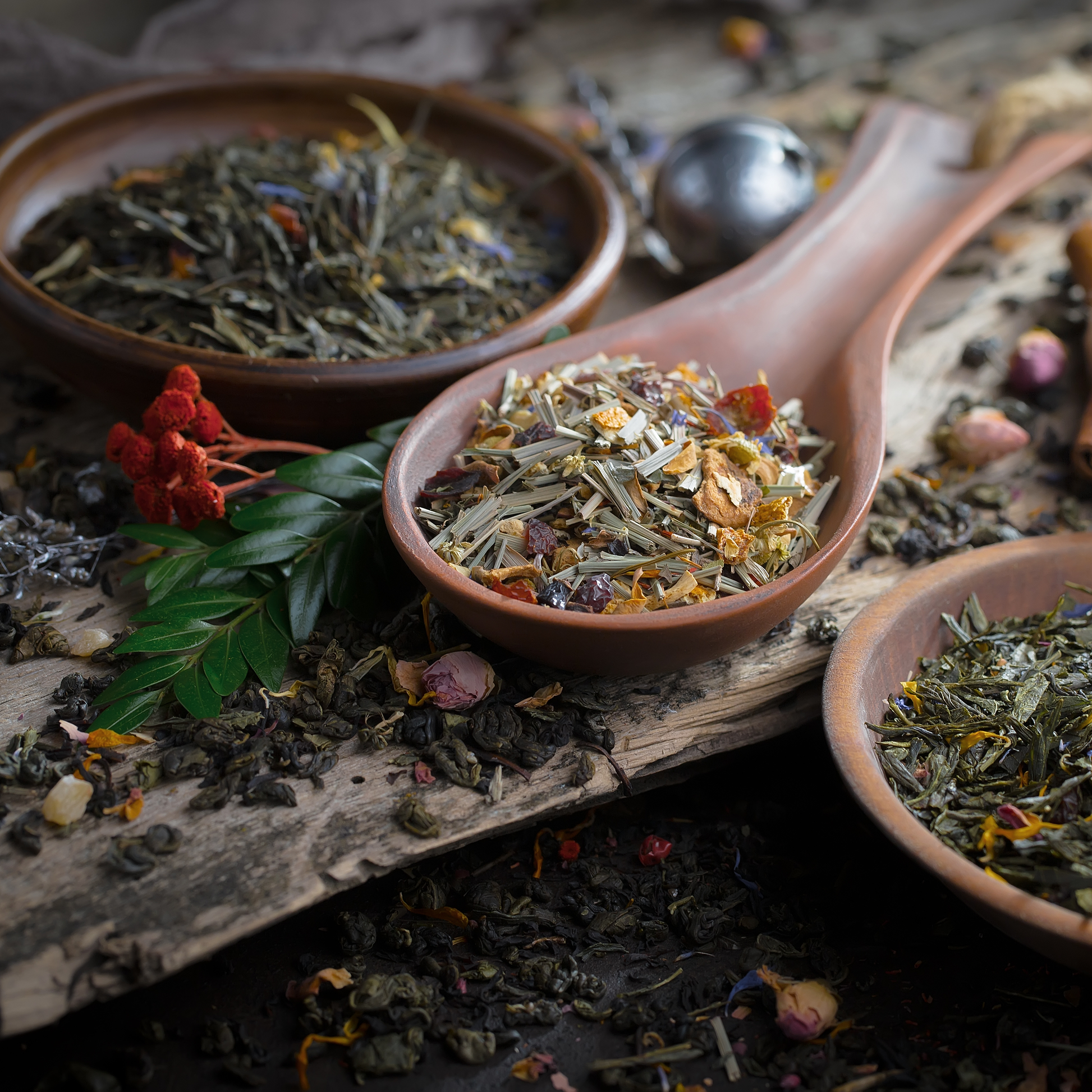 Herbs scattered on a wooden board with some herbs contained in a wooden bowl and a wooden spoon.
